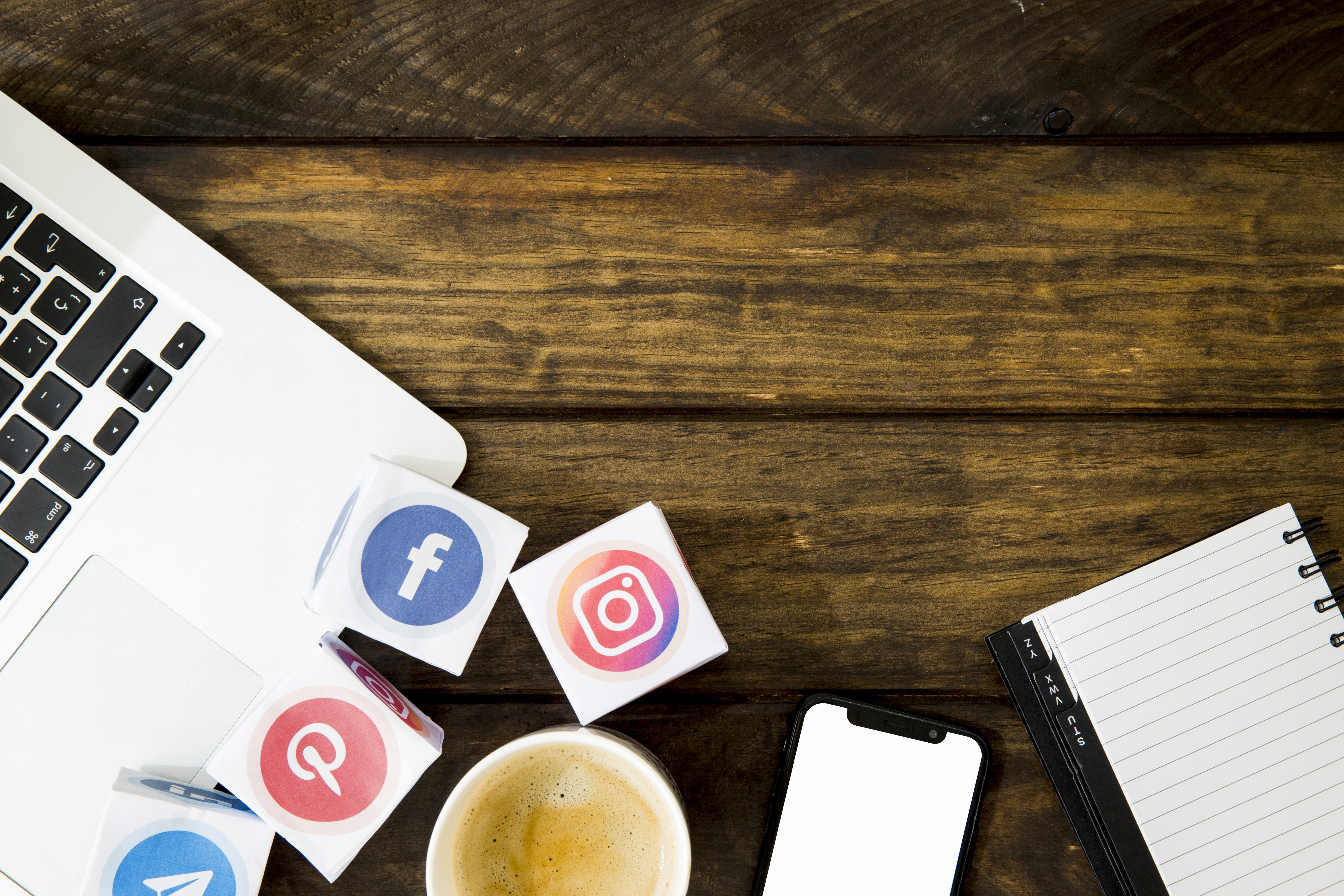 Bureau avec un ordinateur portable, un carnet de note, une tasse à café, un portable et des logos de réseaux sociaux